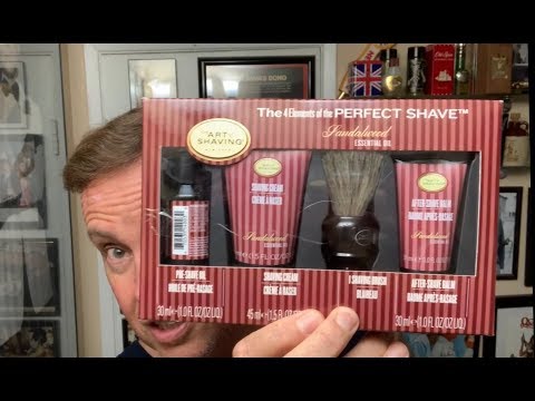 Close-up of The Art of Shaving Sandalwood Perfect Shave Kit held in hand, displaying the pre-shave oil, shaving cream, shaving brush, and after-shave balm