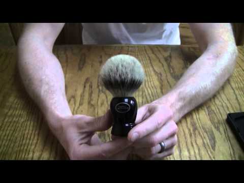 Close-up of hands holding an Art of Shaving badger hair shaving brush resting on a wooden table